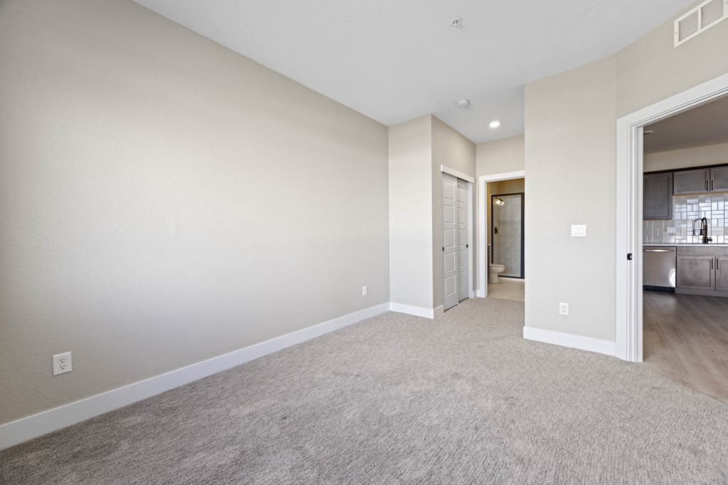 A spacious living room with a carpeted floor and a doorway leading to another room.