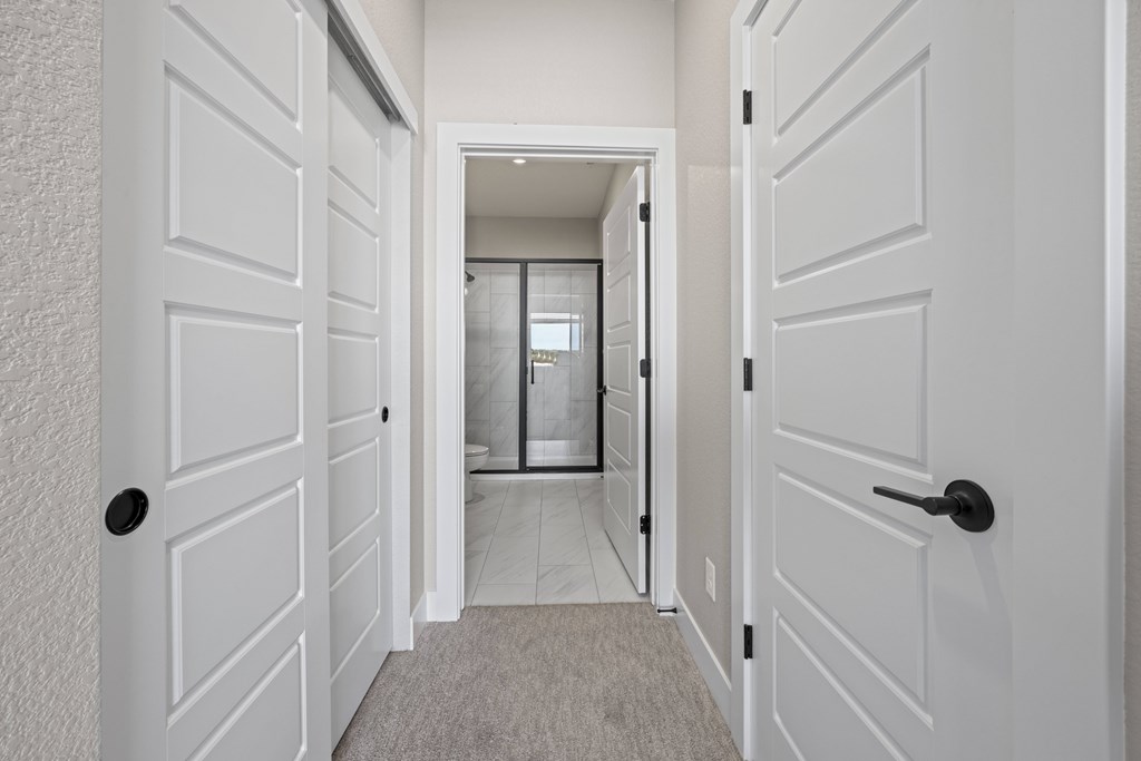 A hallway with white doors and a carpeted floor.