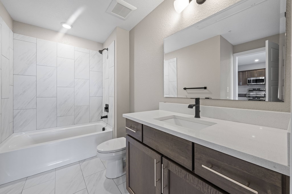 A white bathroom with a marble tile shower and a white bathtub.