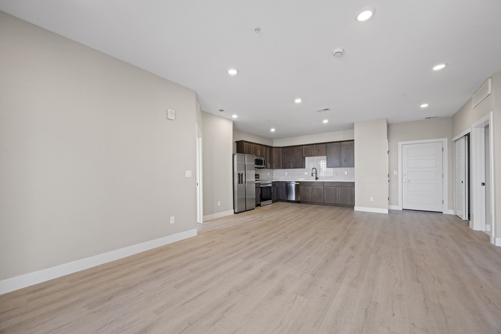 A spacious room with wooden flooring and a kitchen area in the background.