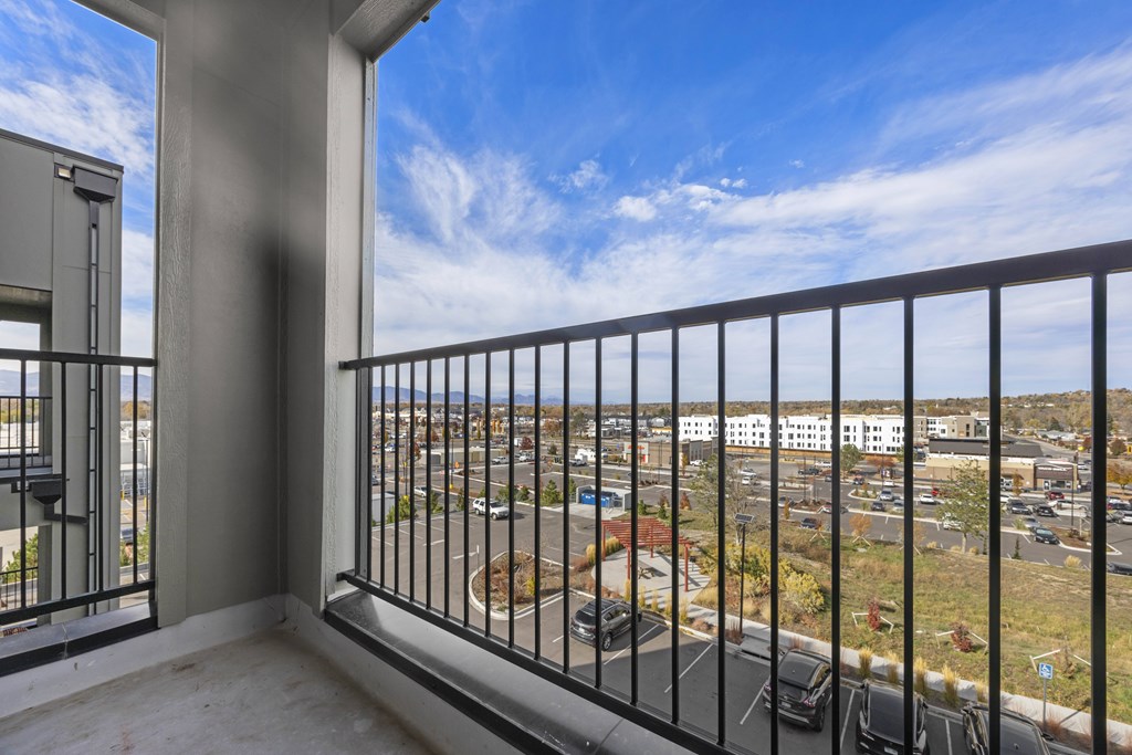 A balcony with a metal railing overlooks a parking lot and buildings.
