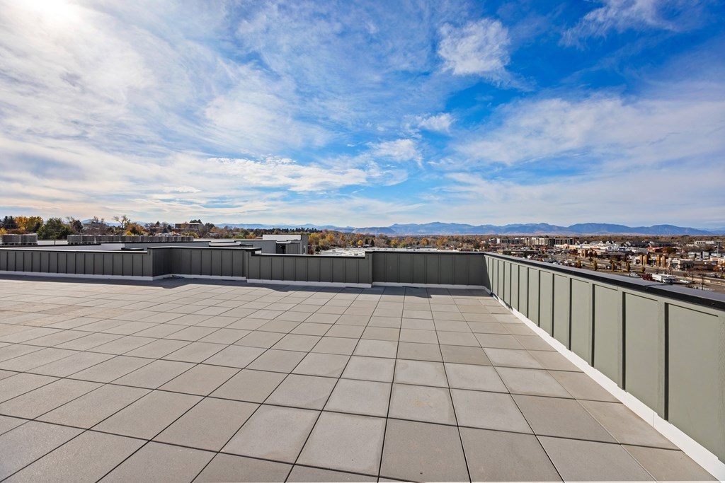 A rooftop with a tiled surface and a cityscape in the distance under a blue sky with clouds.
