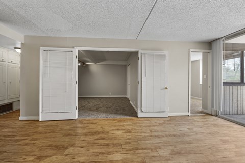 A room with a wooden floor and white walls, with a door open to reveal a carpeted area.