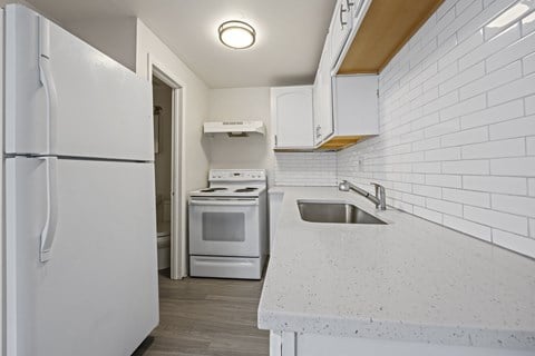 A white kitchen with a refrigerator, oven, and sink.