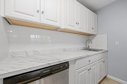 A kitchen with white cabinets and a marble countertop.
