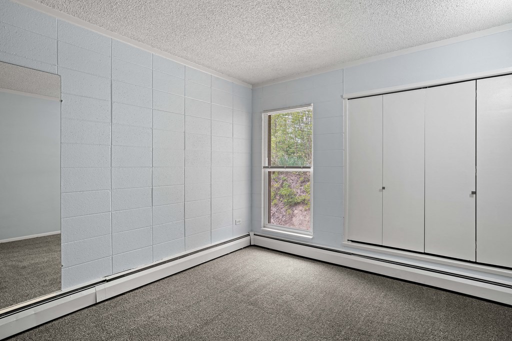 an empty bedroom with a window and two closets