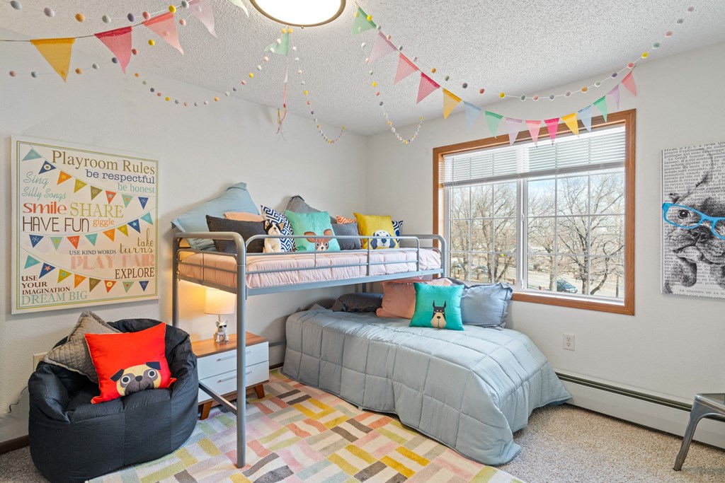 a bedroom with a bunk bed and a chair in front of a window