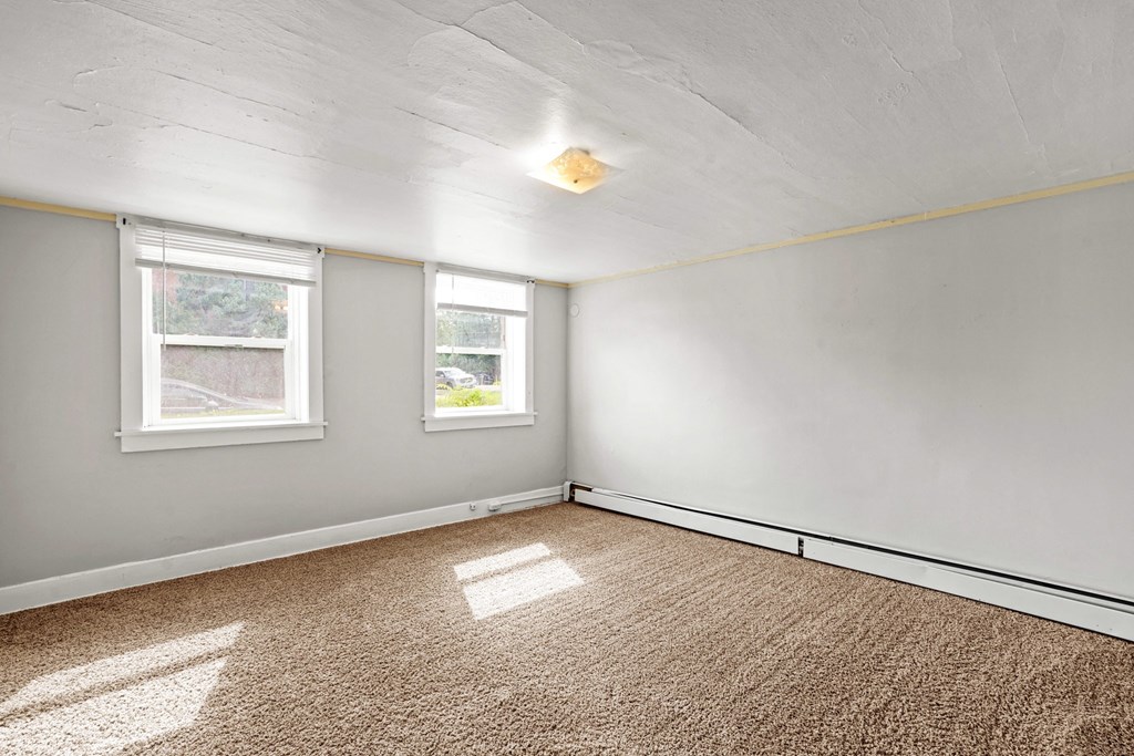 A room with carpeted floor and two windows.