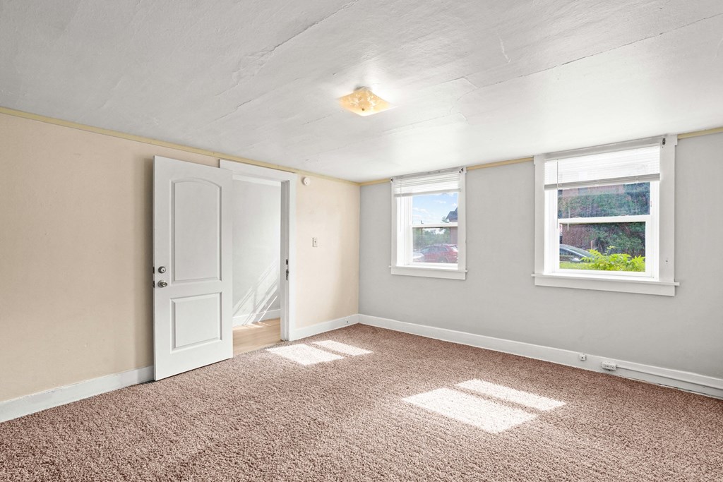 A room with a carpeted floor, a door, and a window.