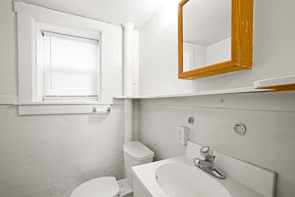 A bathroom with a toilet, sink, and mirror.
