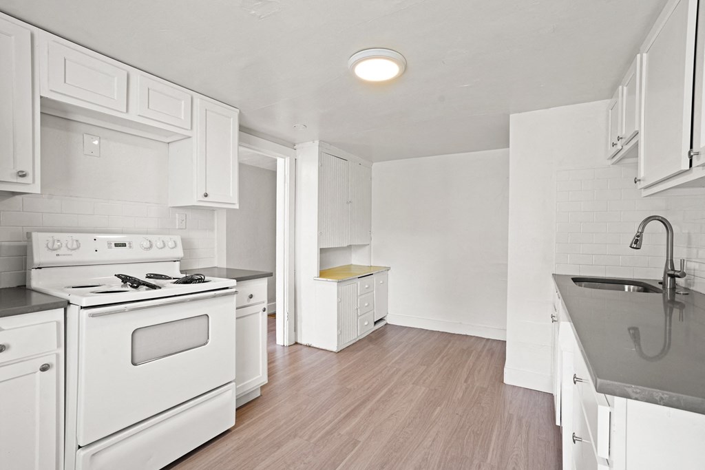 A white kitchen with a stove, sink, and cabinets.