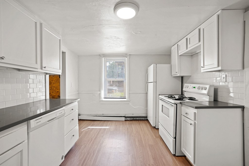 A white kitchen with wood floors and white appliances.