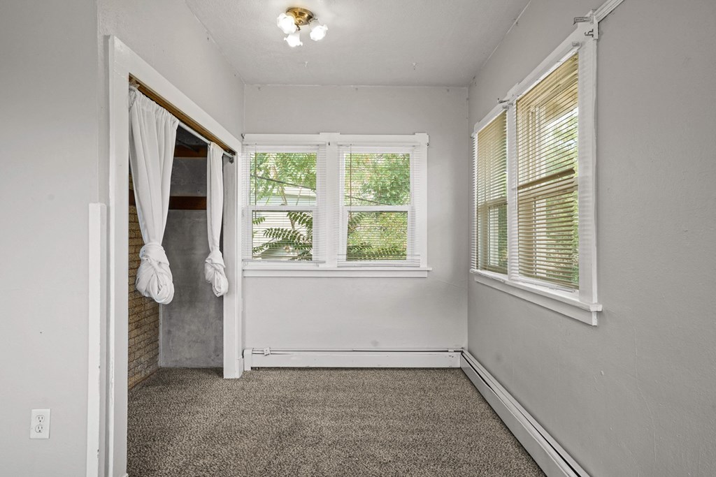 A room with a carpeted floor, a window with blinds, and a door with a curtain hanging on it.