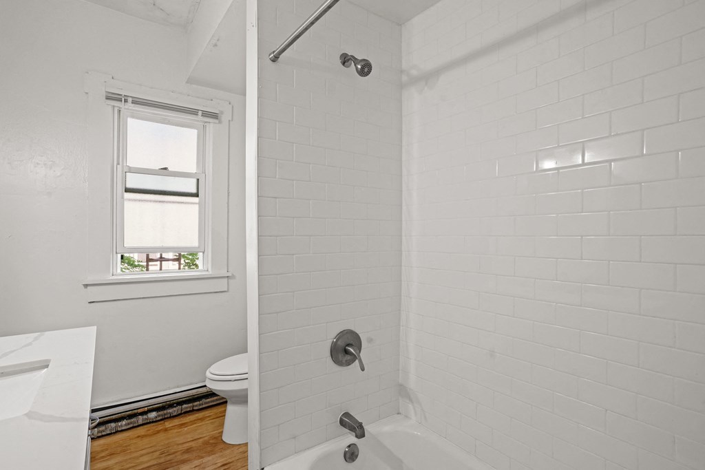 A white bathroom with a toilet, tub, and window.