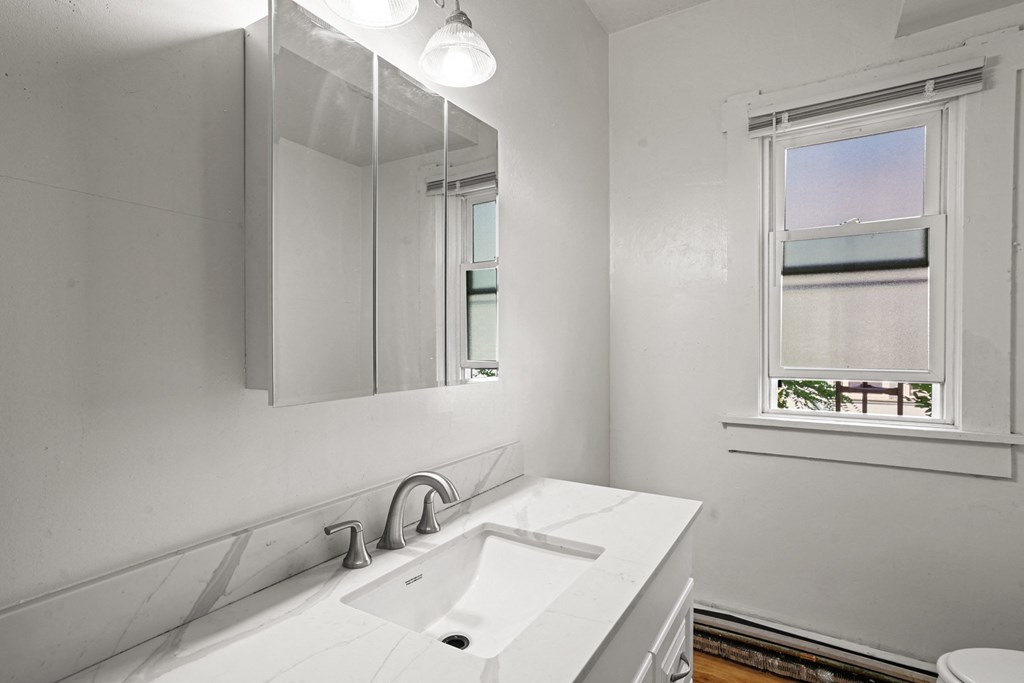 A white bathroom with a sink, mirror, and window.