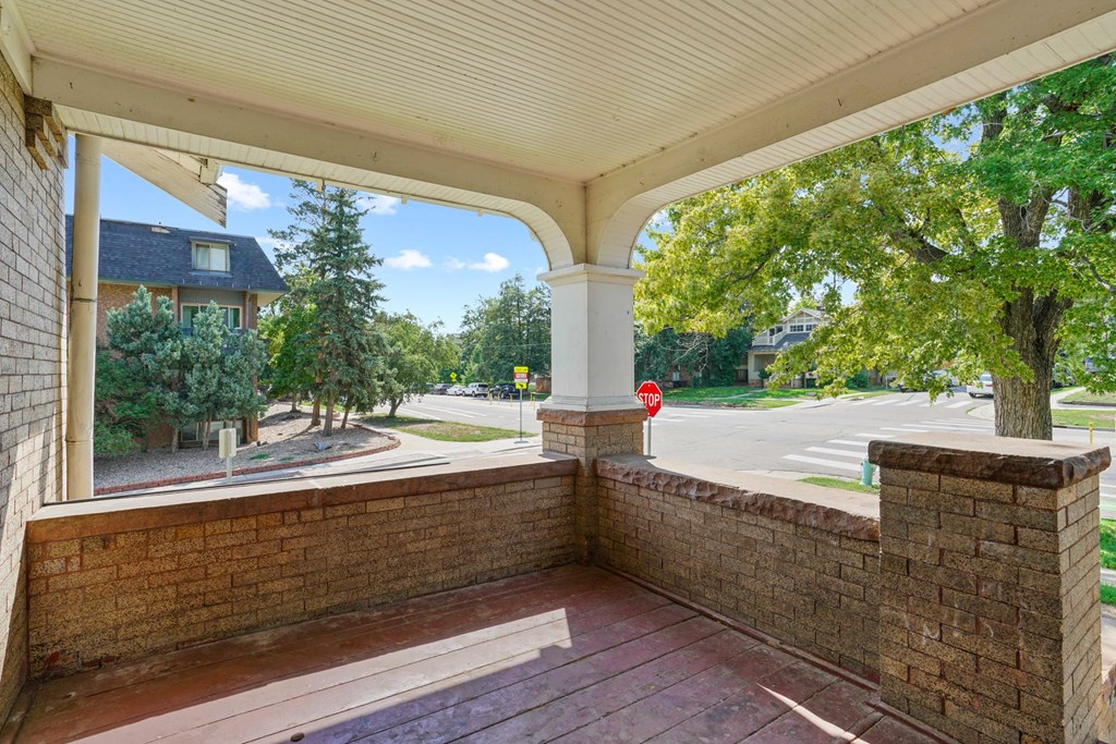 A covered porch with a red brick wall and a stop sign in the background.