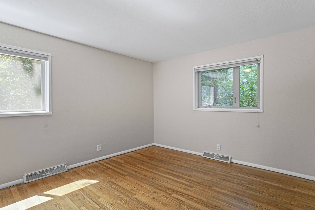a bedroom with two windows and a hardwood floor