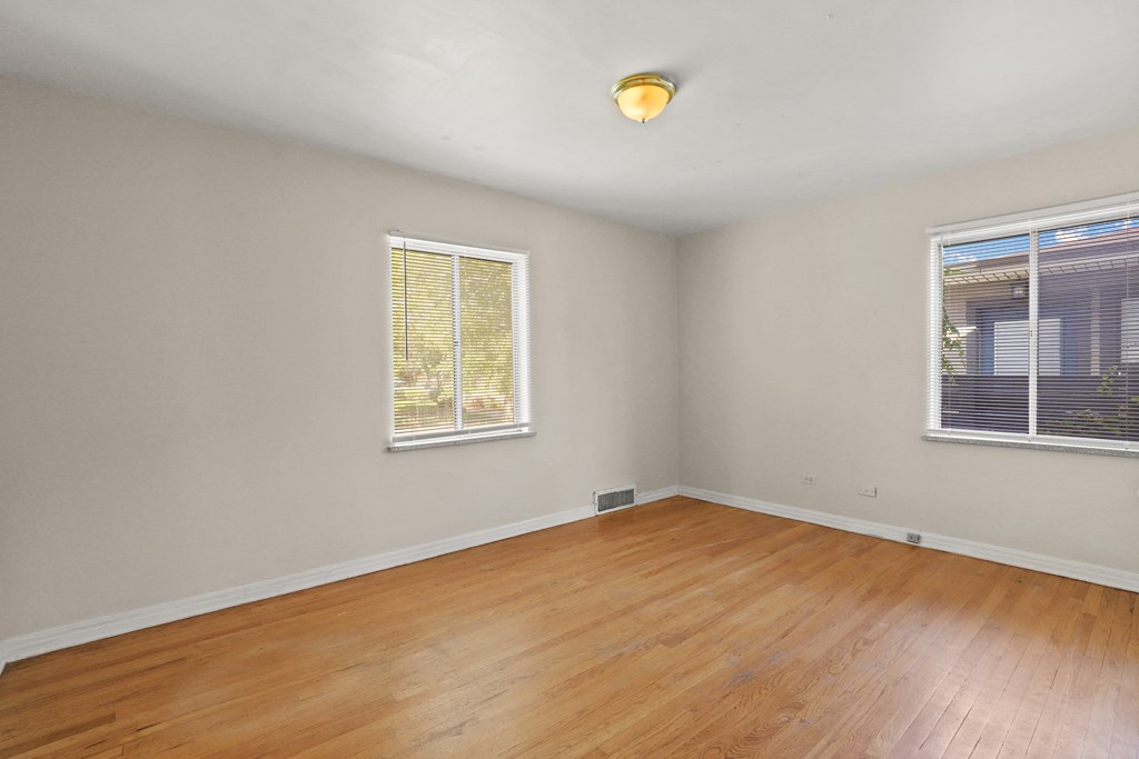 an empty room with wood floors and two windows