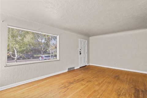 an empty living room with a large window and wooden floors