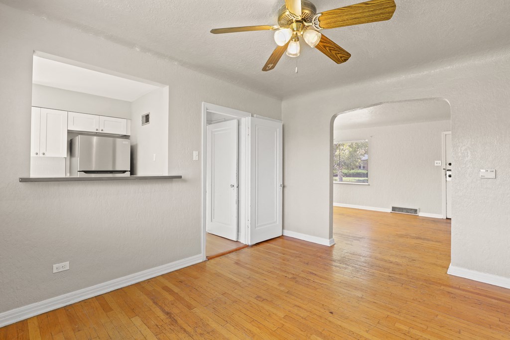 an empty living room with a ceiling fan and a kitchen