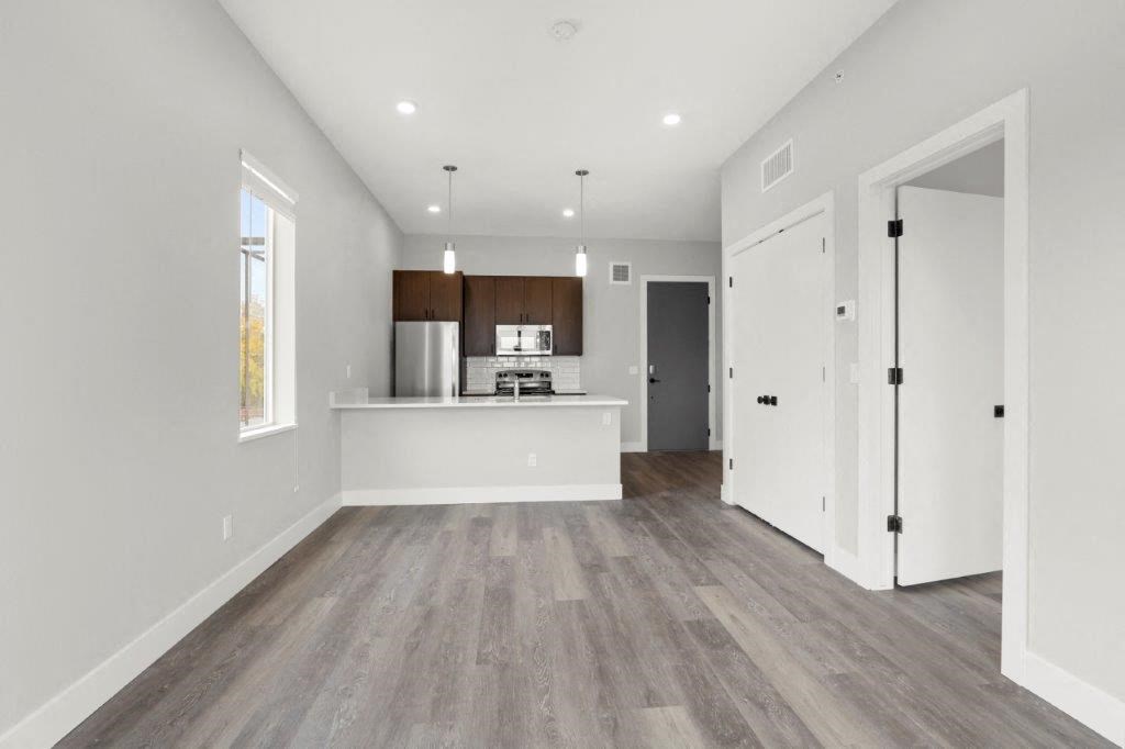 an empty living room with a kitchen in the background