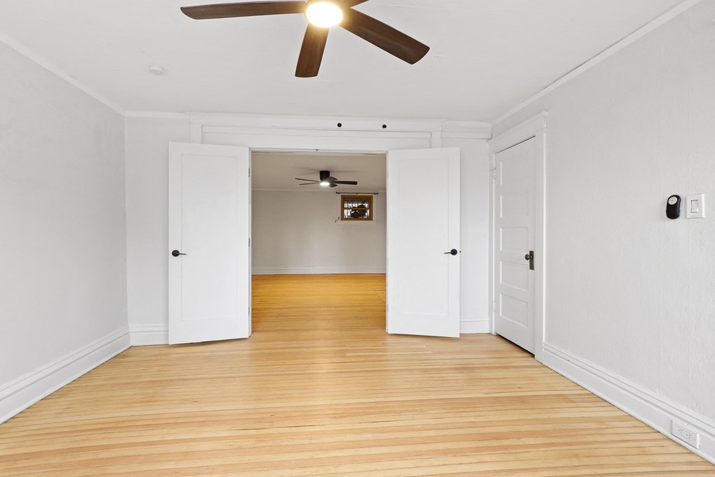a living room with white walls and wood floors and a ceiling fan