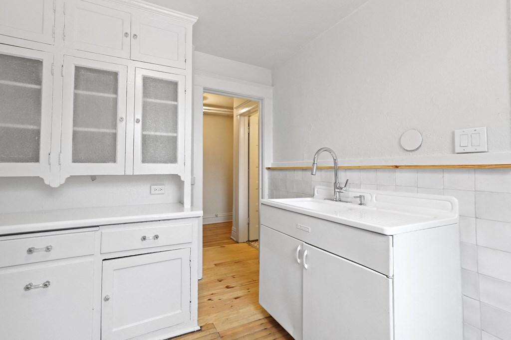 a kitchen with white cabinets and a sink and a door to a hallway