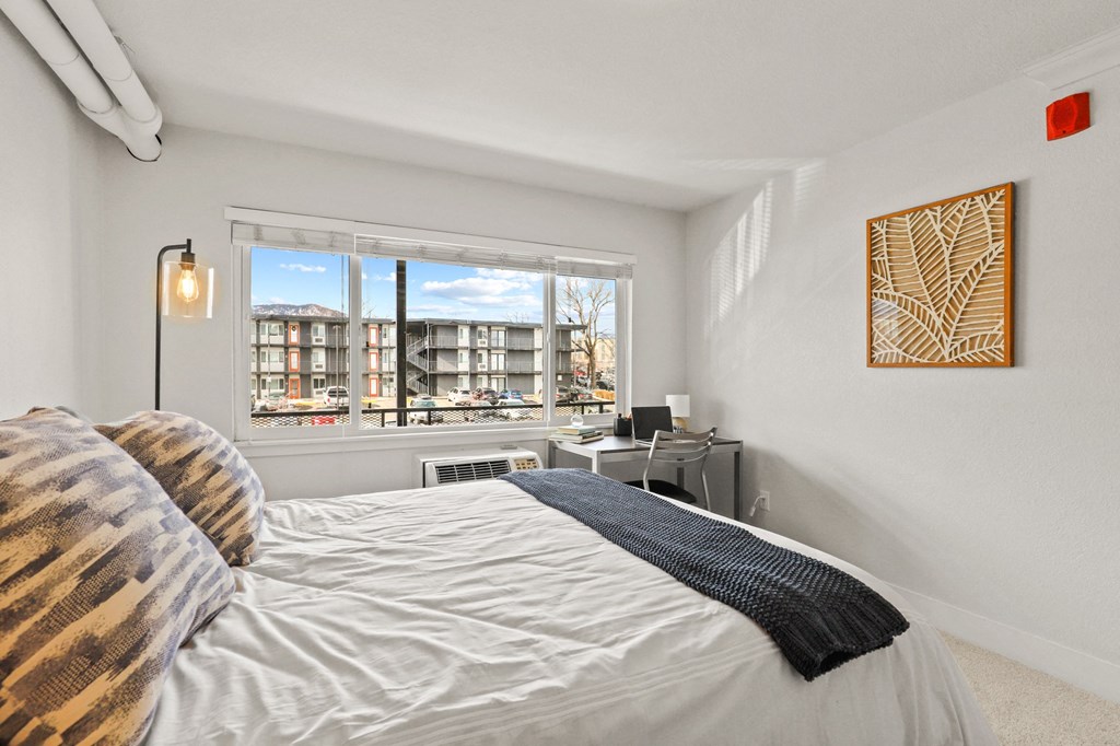 a bedroom with a large window and a bed and a desk