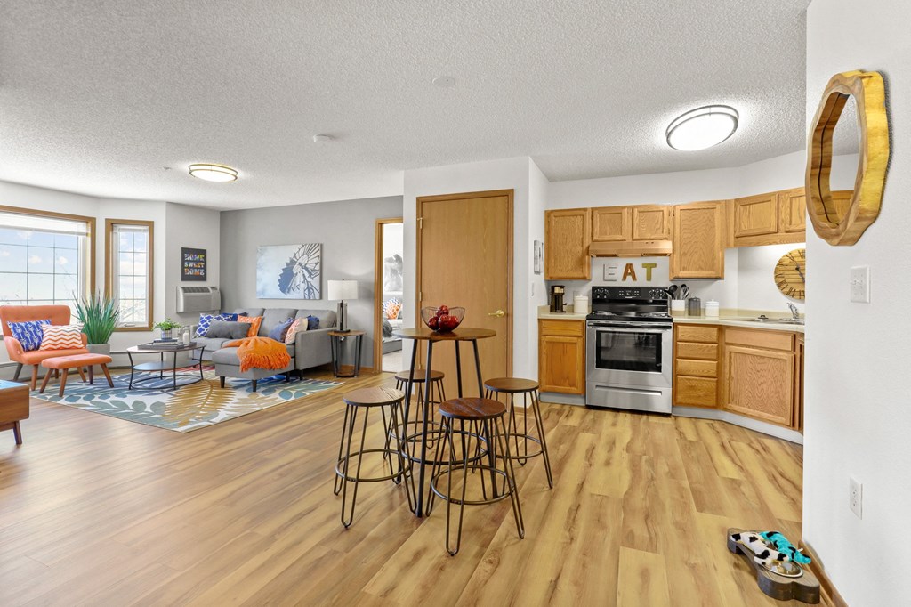 the view of a living room and a kitchen with wooden floors and wooden cabinets