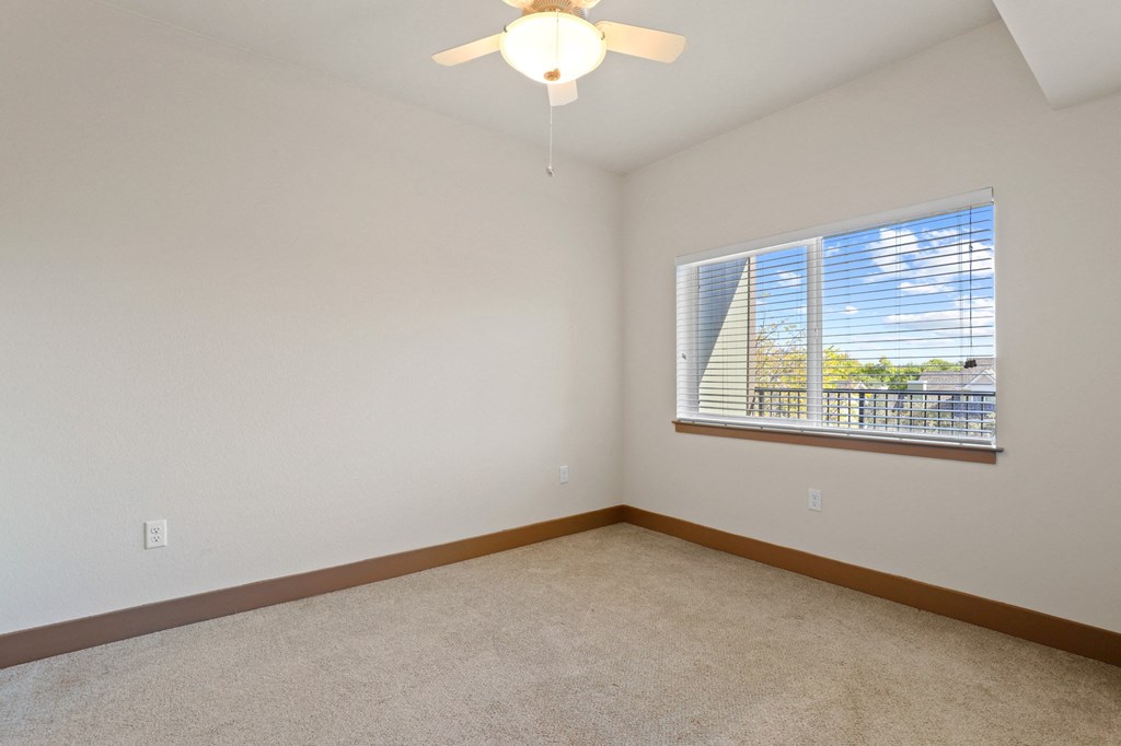 an empty bedroom with a large window and a ceiling fan