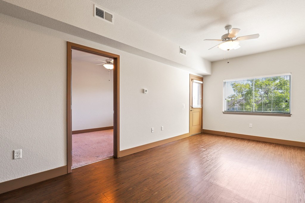 an empty living room with wood floors and a ceiling fan
