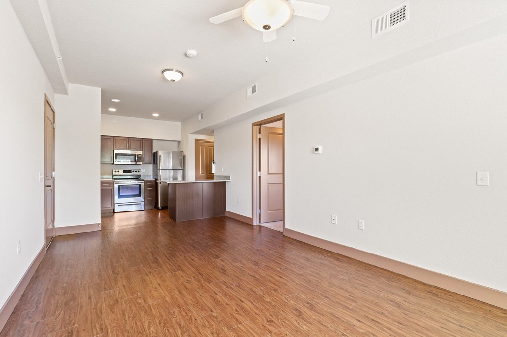 an empty living room and kitchen with wood flooring and a ceiling fan