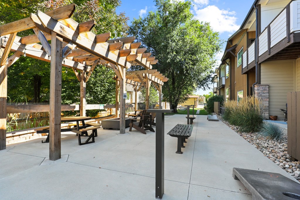 a patio with benches and a pergola in front of a building with trees