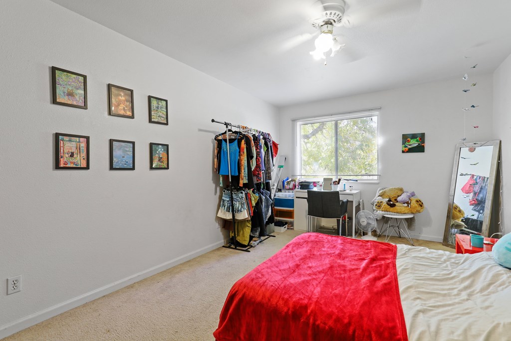 A bedroom with a red bedspread and a clothing rack with clothes hanging on it.
