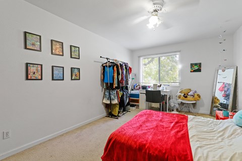 A bedroom with a red bedspread and a clothing rack with clothes hanging on it.