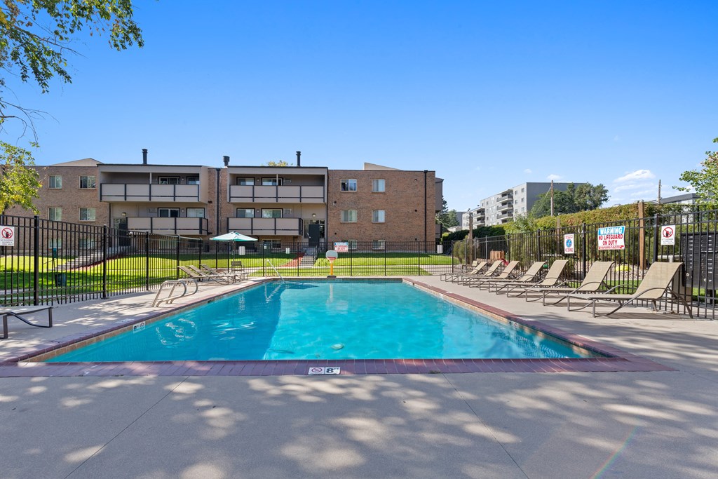 A swimming pool surrounded by chairs and a building in the background.