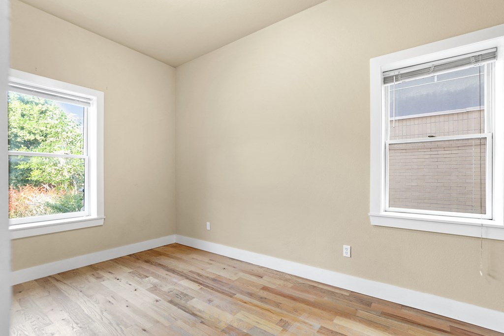 a bedroom with two windows and a hardwood floor