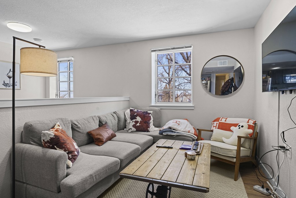 A living room with a grey couch, a wooden coffee table, and a round mirror on the wall.