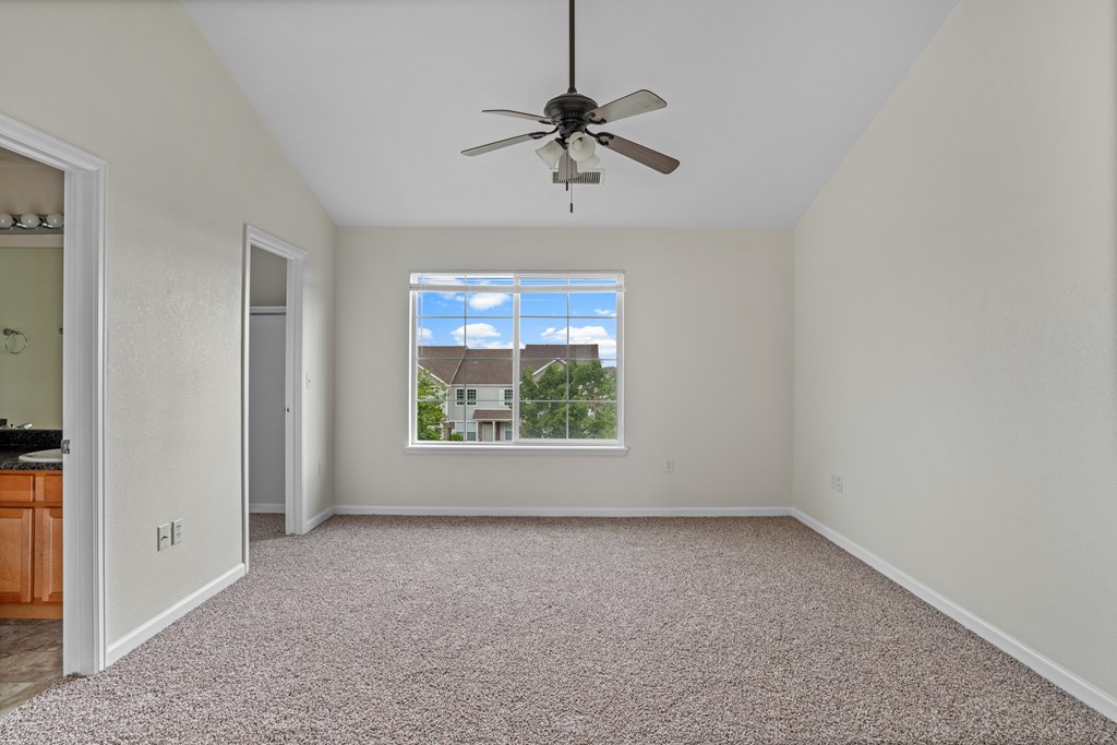 A room with a ceiling fan and a window showing a house outside.