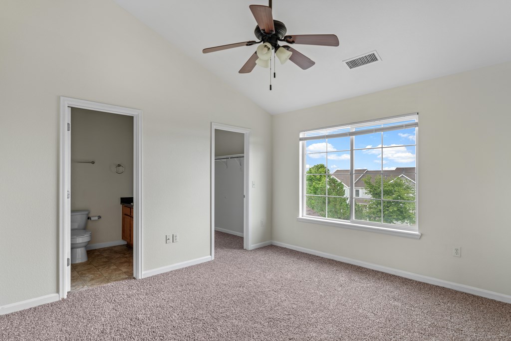 A room with a ceiling fan and a window overlooking a house.