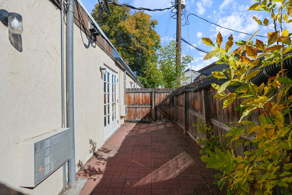 A narrow alley with a brick pathway and a wooden fence on the right side.