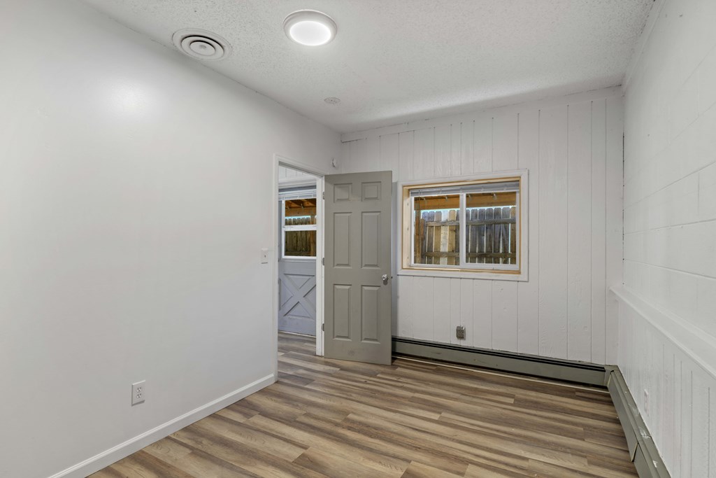 A room with a grey door and a window with white curtains.