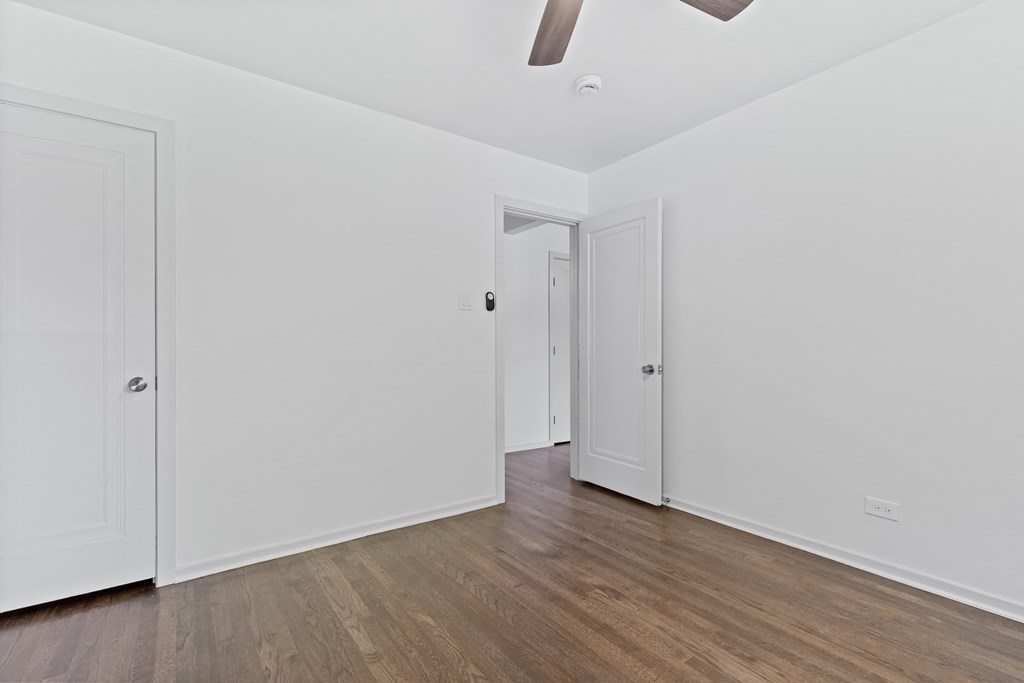 a bedroom with white walls and wood floors and a closet