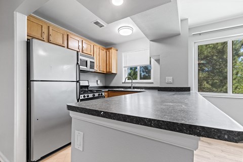 A kitchen with a black countertop and a stainless steel refrigerator.
