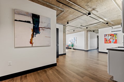 A large painting hangs on a white wall in a spacious room with wooden floors and exposed ceiling beams.