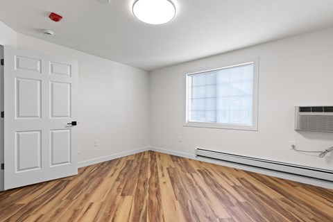 A room with a white door, a window, and a wooden floor.