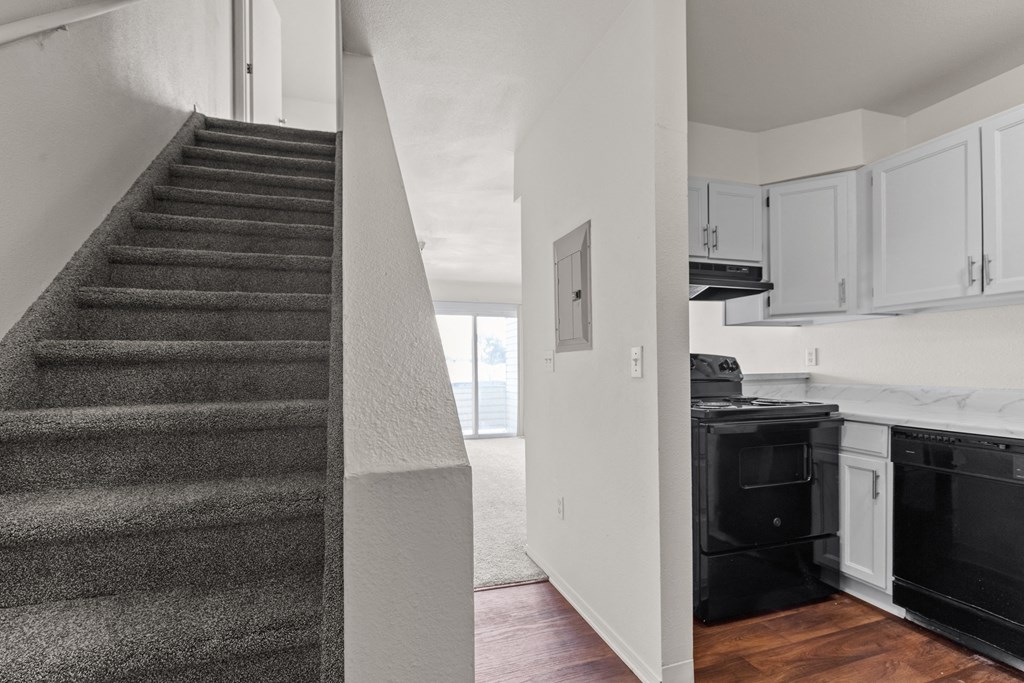 A staircase leads to a kitchen area with white cabinets and black appliances.