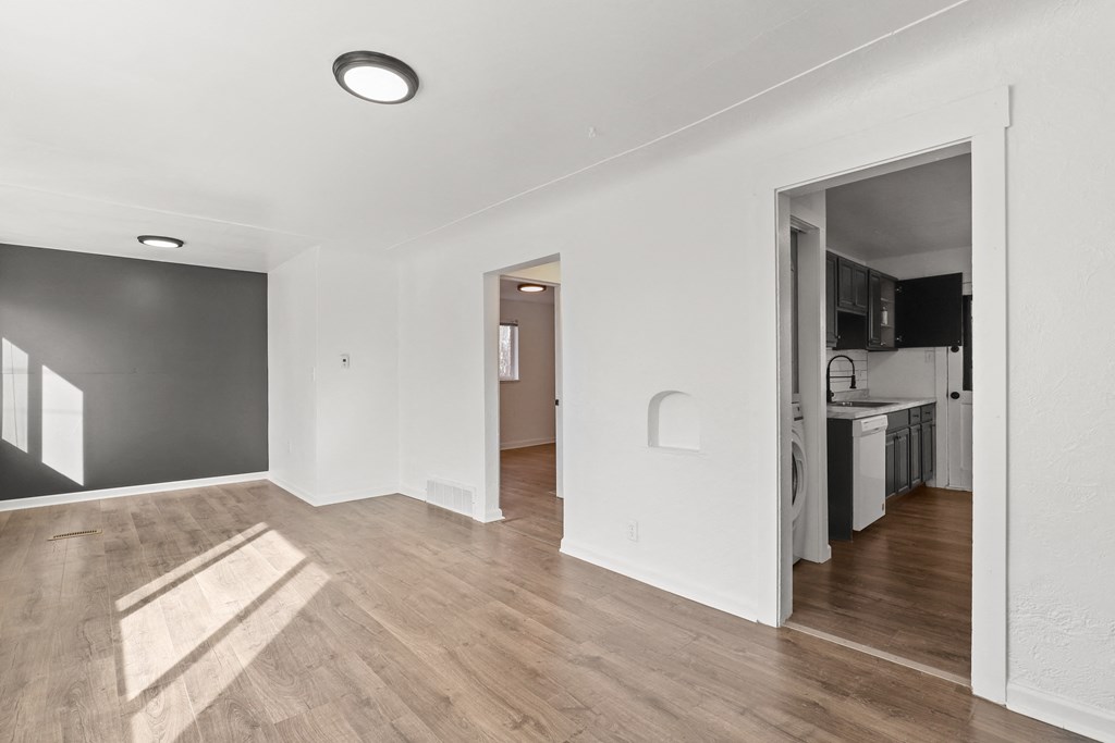 a renovated living room and kitchen with white walls and wood floors