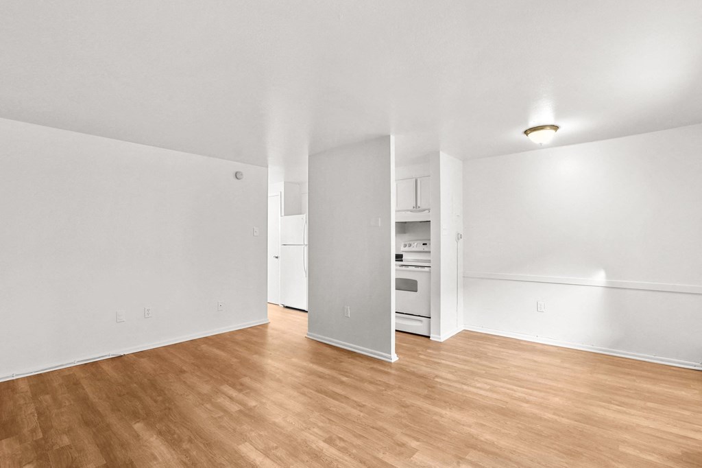the living room of an apartment with wood flooring and white walls