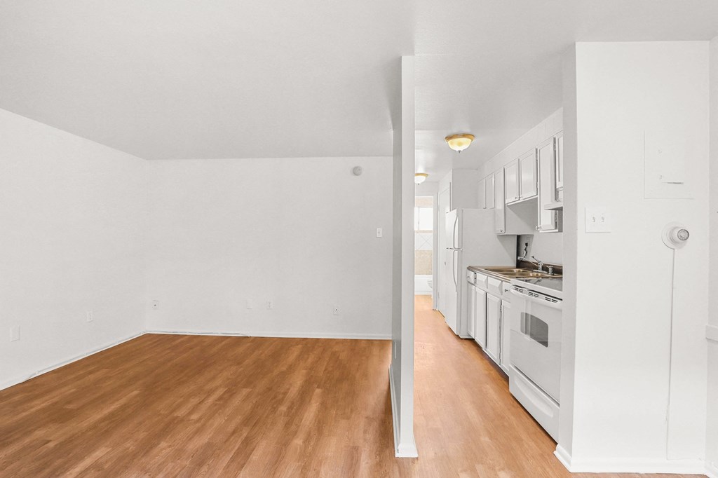 the living room and kitchen of an apartment with white walls and wood flooring